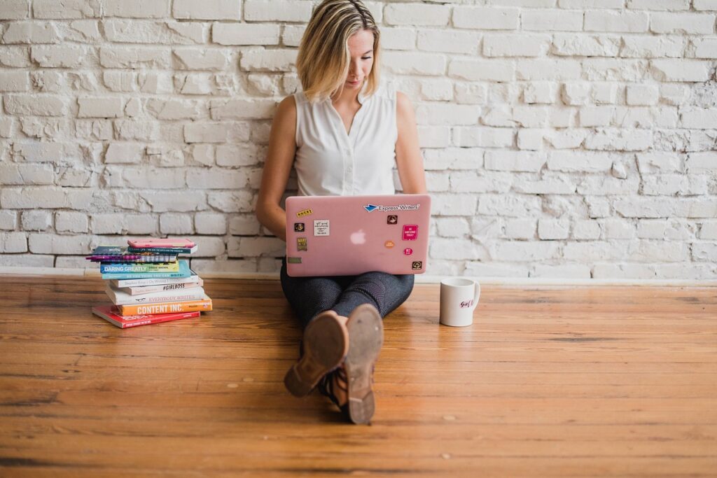 A woman sitting on the floor using a pink laptop